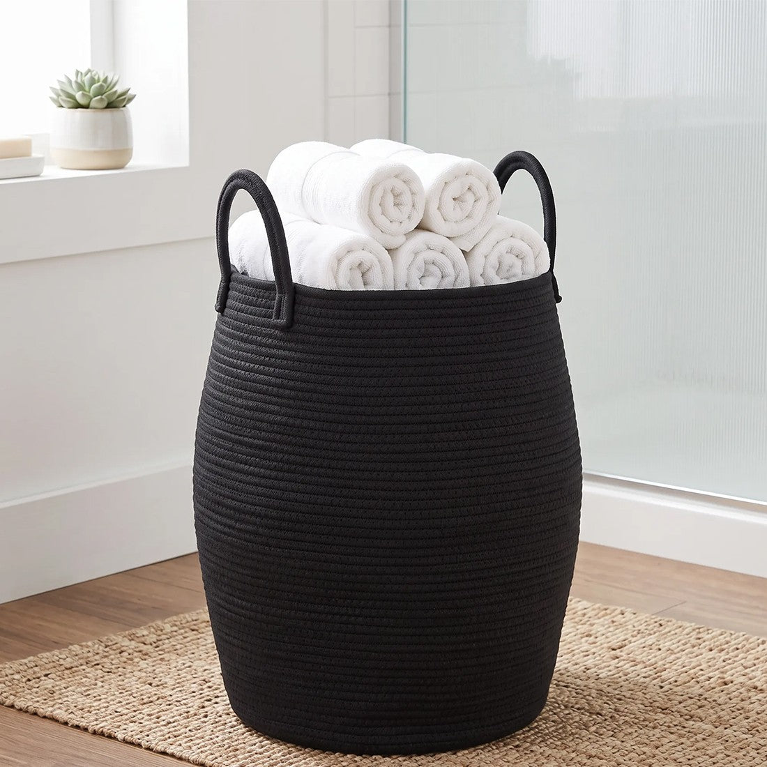 Tall black rope laundry basket topped with rolled white towels