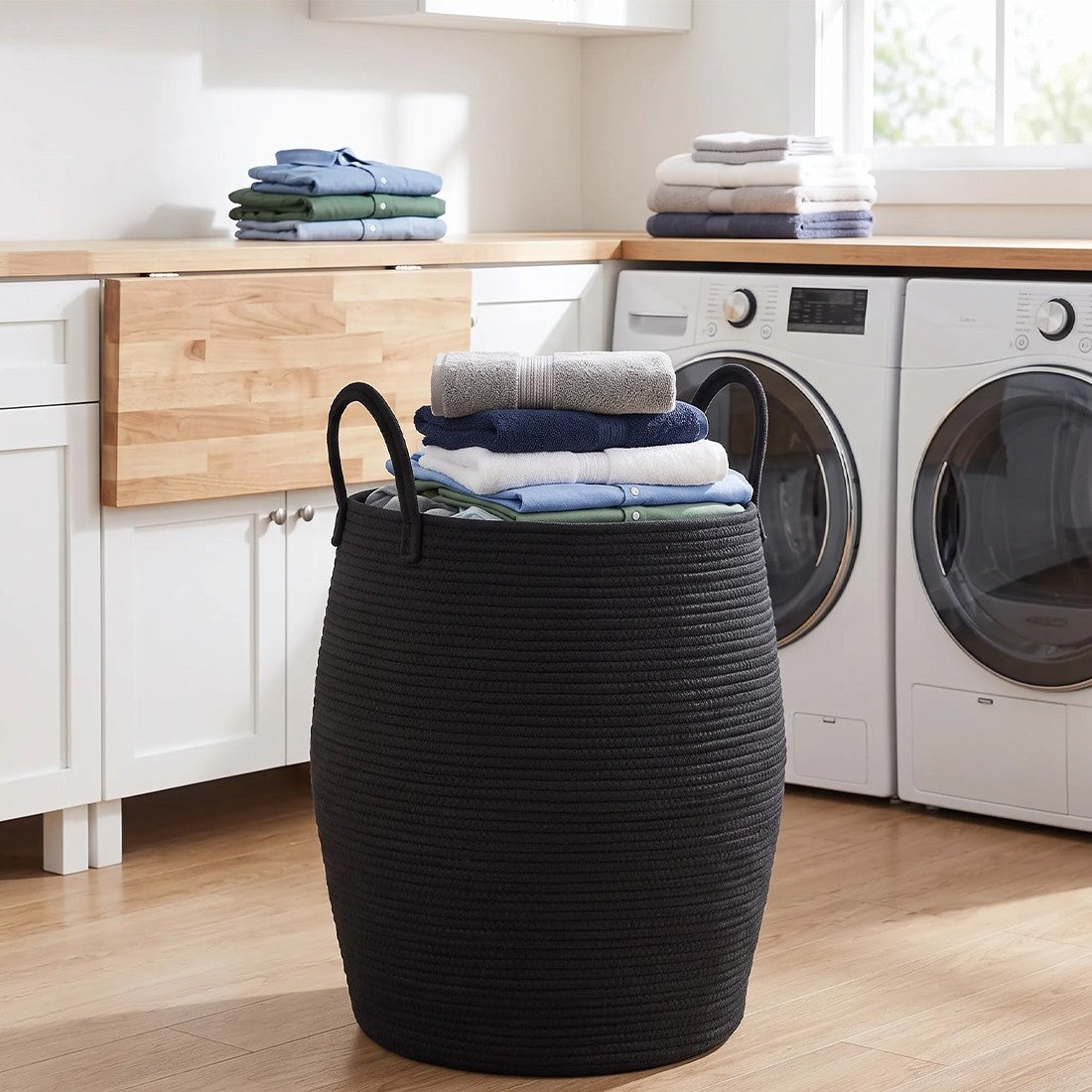 Black rope laundry basket filled with folded clothes beside a washing machine