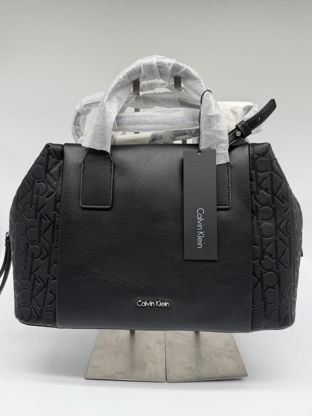 Black Calvin Klein Misha duffle bag with CK monogram, strap, and dust bag, featuring a sleek design and new with tags.