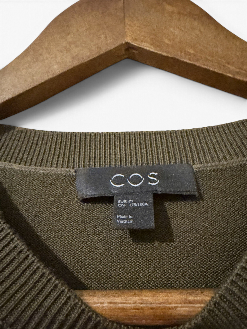 Men's COS olive green wool crew neck jumper, size M, showing the soft knit fabric and classic fit on a hanger.