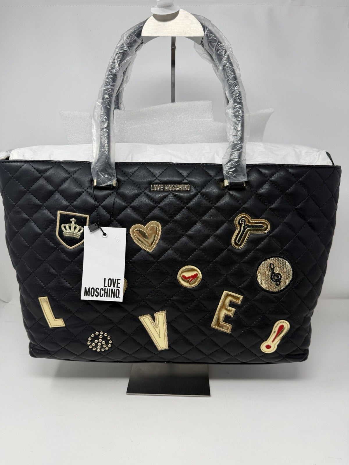 Love Moschino black quilted faux leather tote with gold LOVE appliqué patches, front view with swing tag